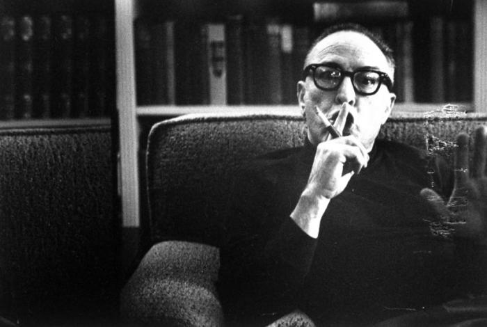 Screen writer and director Dalton Trumbo holding finger up to lips as if to say quiet, and waving other hand while sitting on sofa. (Photo by John Swope/The LIFE Images Collection/Getty Images)